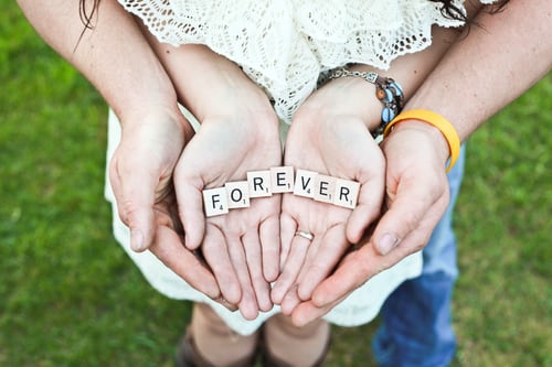 A couple wtih cupped hands holding a sign that says forever.