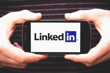 Hands holding a mobile phone with LinkedIn's logo