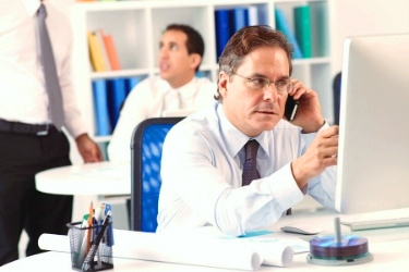 Man talking through the phone pointing at the computer screen