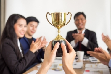 Someone at the table holding a trophy while others applaud during a meeting