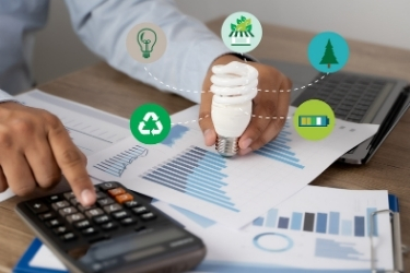 Man holding a eco-friendly lightbulb while using the calculator