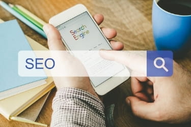 Hand holding a phone with a search bar with the word SEO