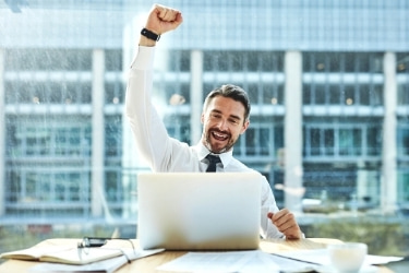 Man celebrating a closed deal in front of his laptop