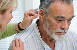 Audiologist fitting a Behind the Ear hearing aid for a hearing loss patient.