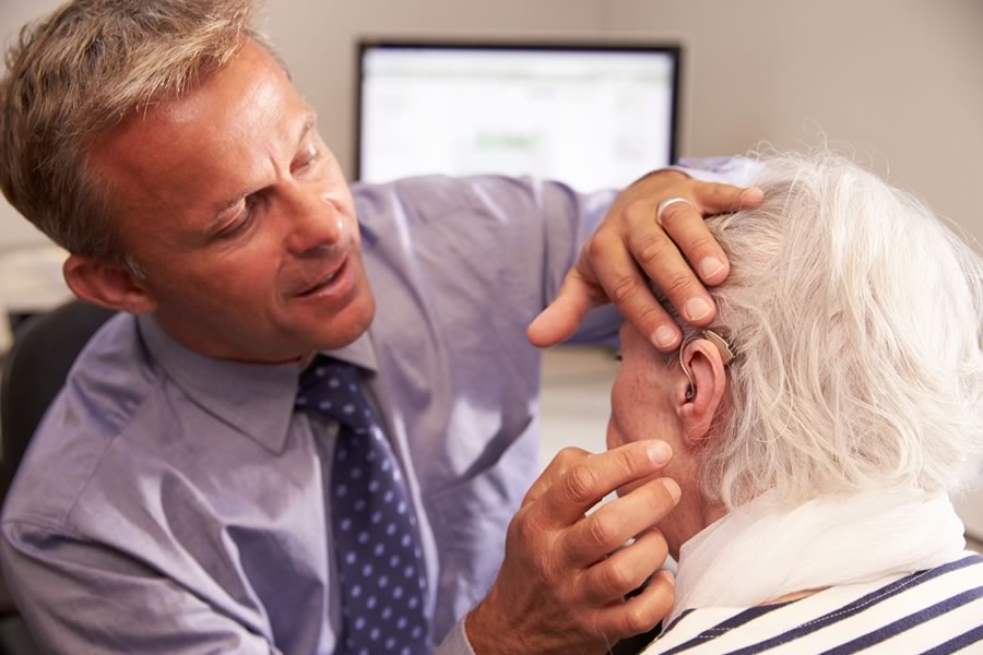 Audiologist fitting a patient with hearing aids