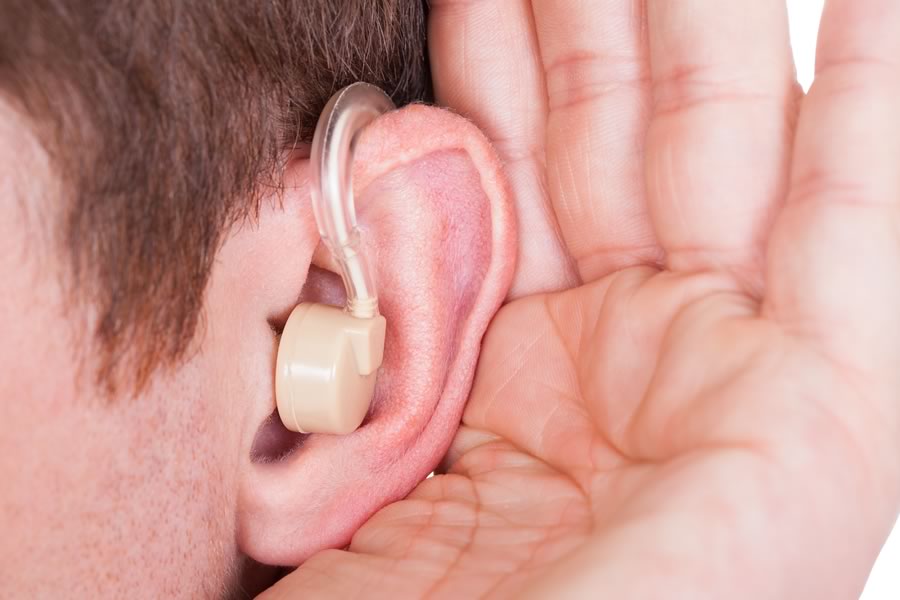 Man with palm cupped behind his ear and hearing aid to boost the reception