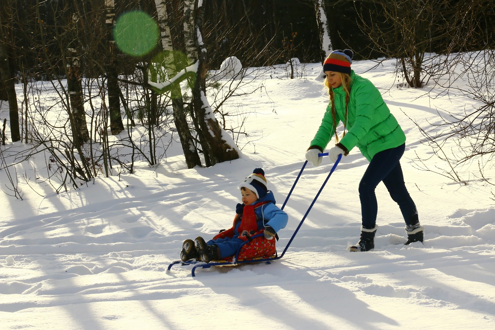 mother pushing child through snow on a sled