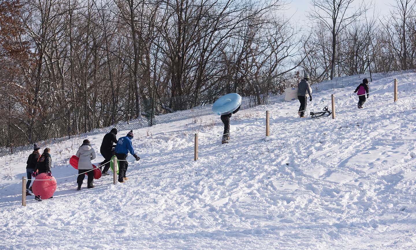 people walking up snow covered hill with sleds & tubes at a Cleveland Metro Park