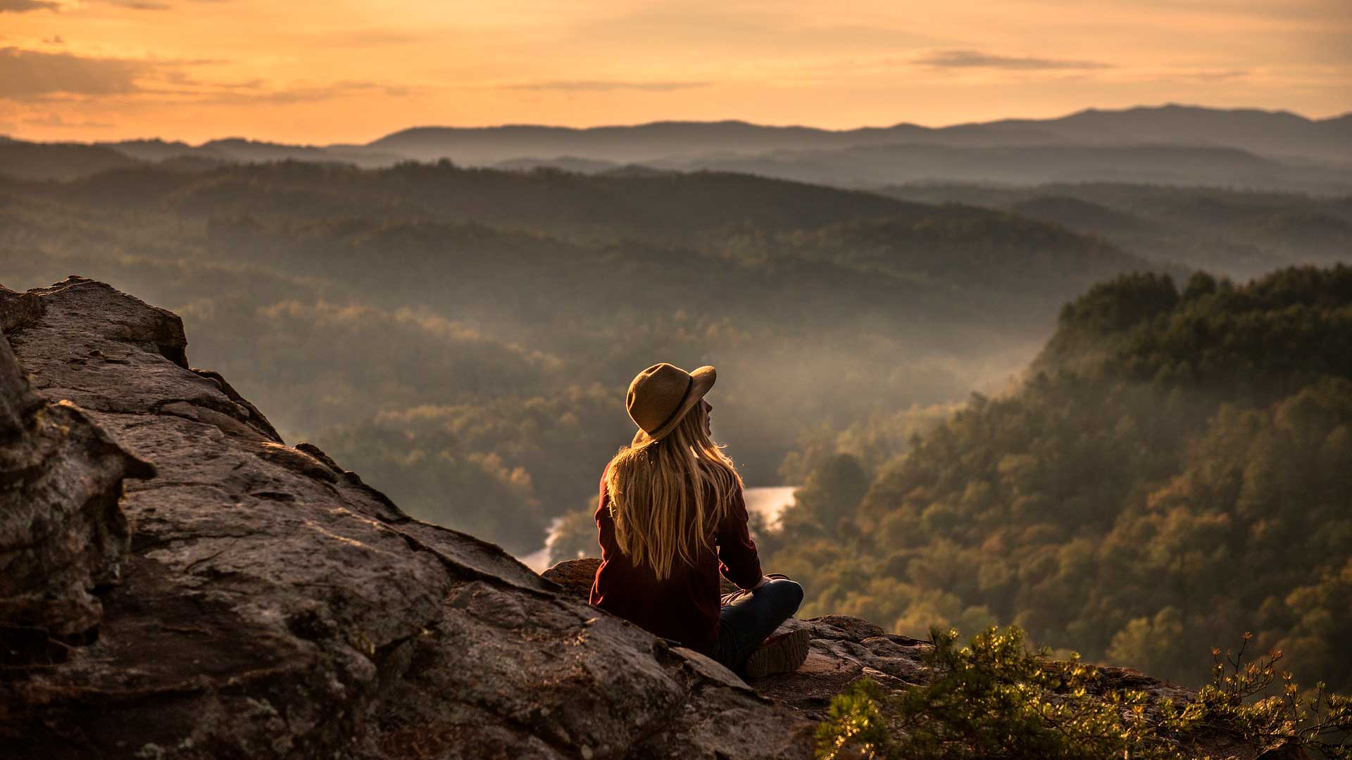 Mulher sentada em montanha observando o pôr do sol no horizonte