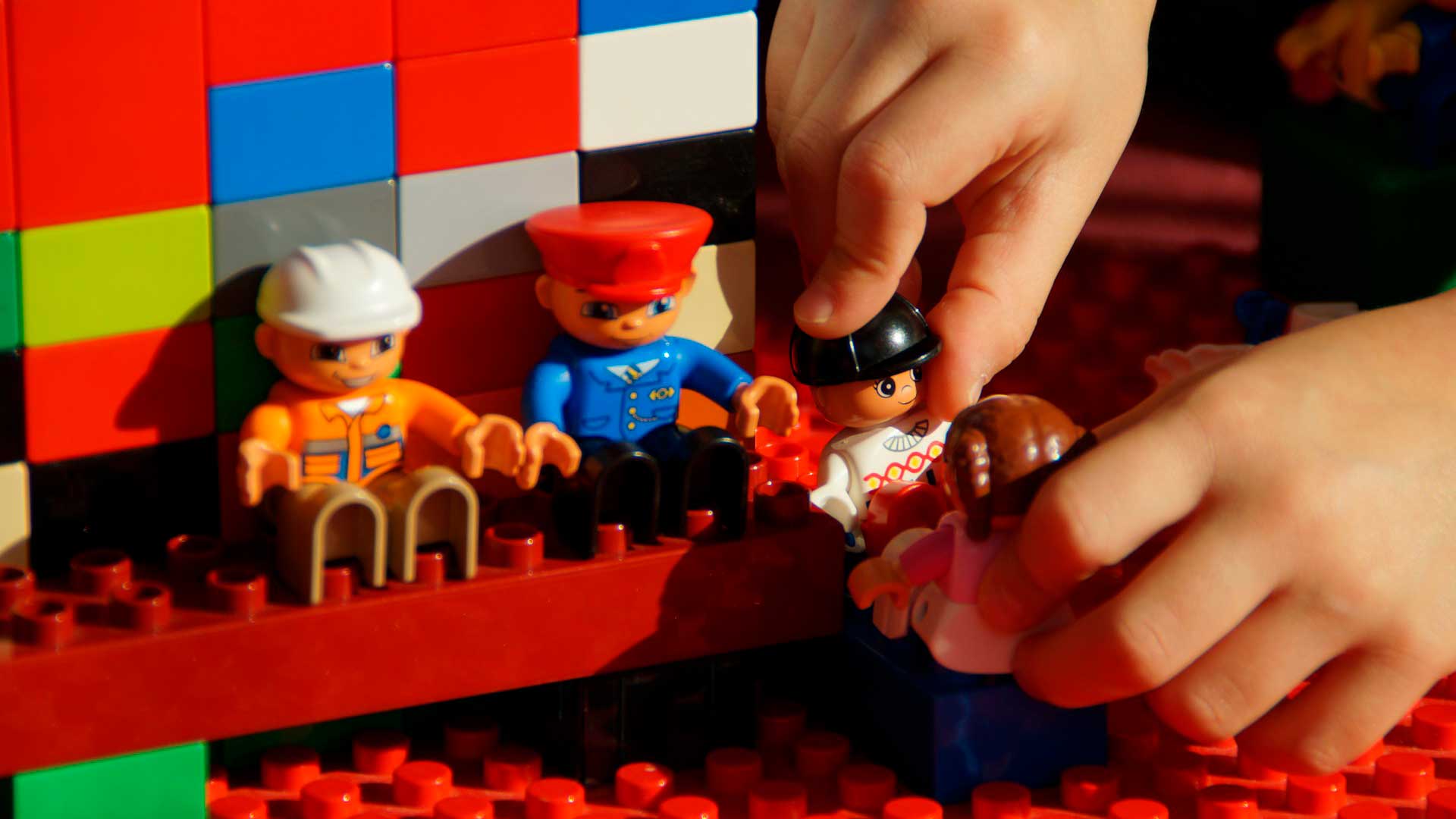 Peças de LEGO com tres bonecos sentado e uma boneca em pé nas mãos da criança