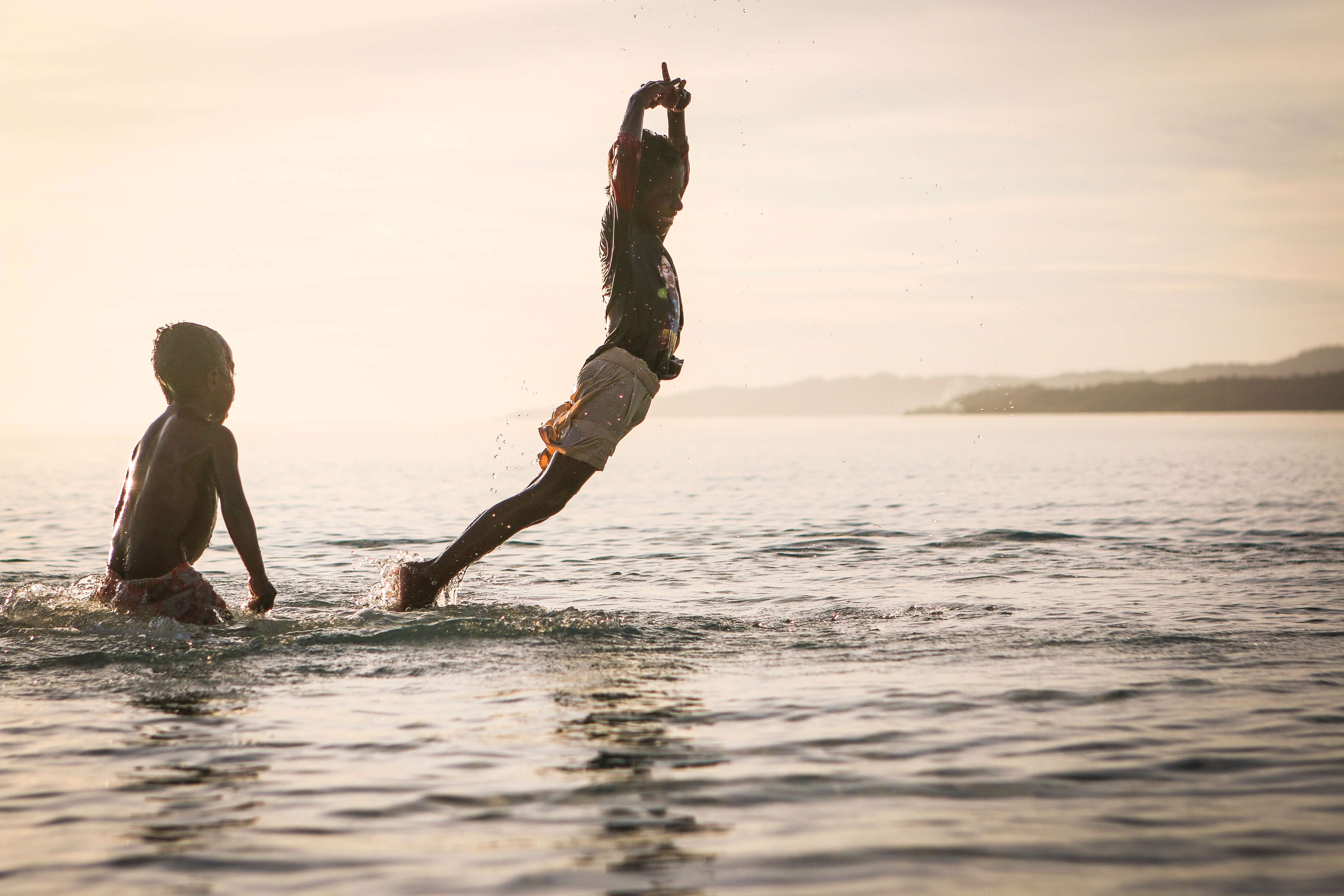 Dois garotos brincando em um lago com o por do sol de fundo.