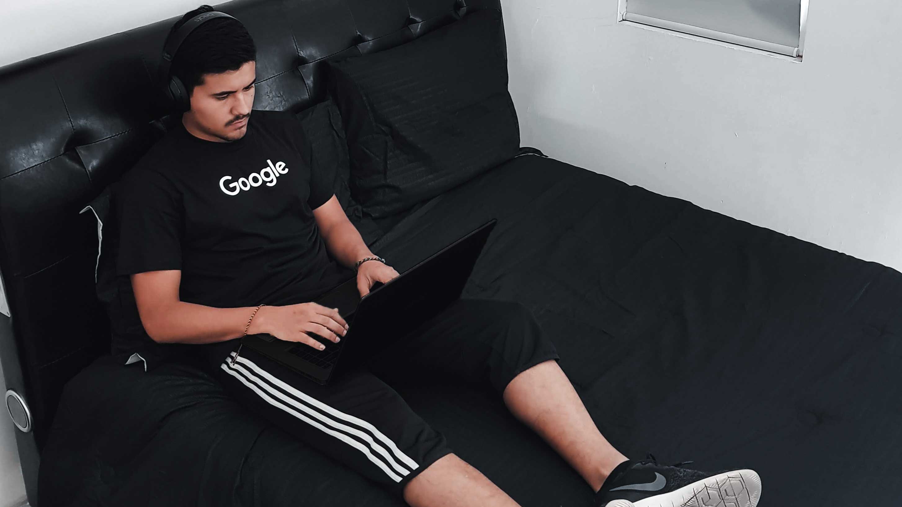 Rapaz sentadoem sofá preto com notebook no colo, em sua camiseta lê-se "Google".