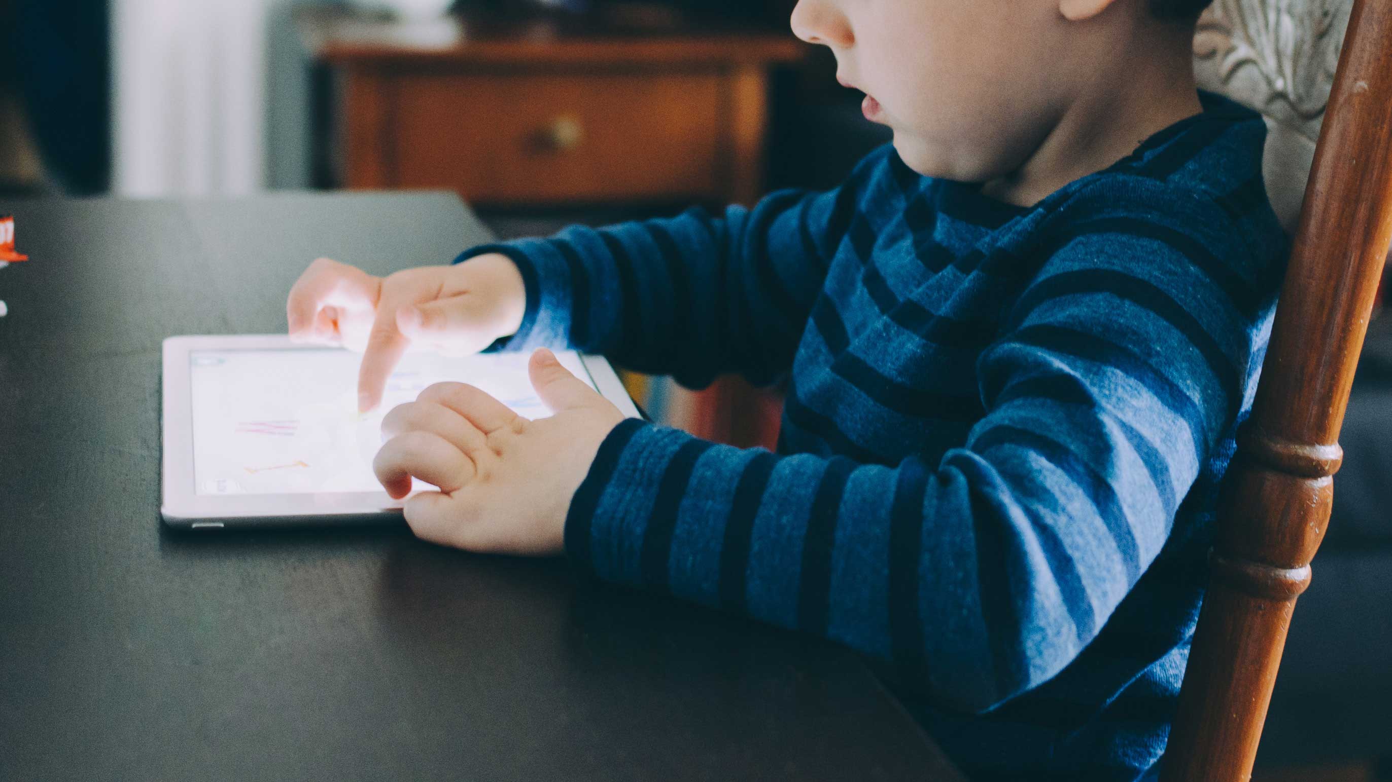 Menino sentado à mesa mexendo em seu tablet 