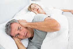 Husband covering his ears because of his wife's snoring.