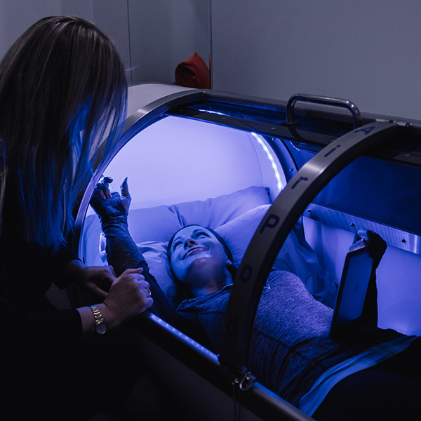 Operator communicating via external control box with person in AirPod capsule during therapy session.