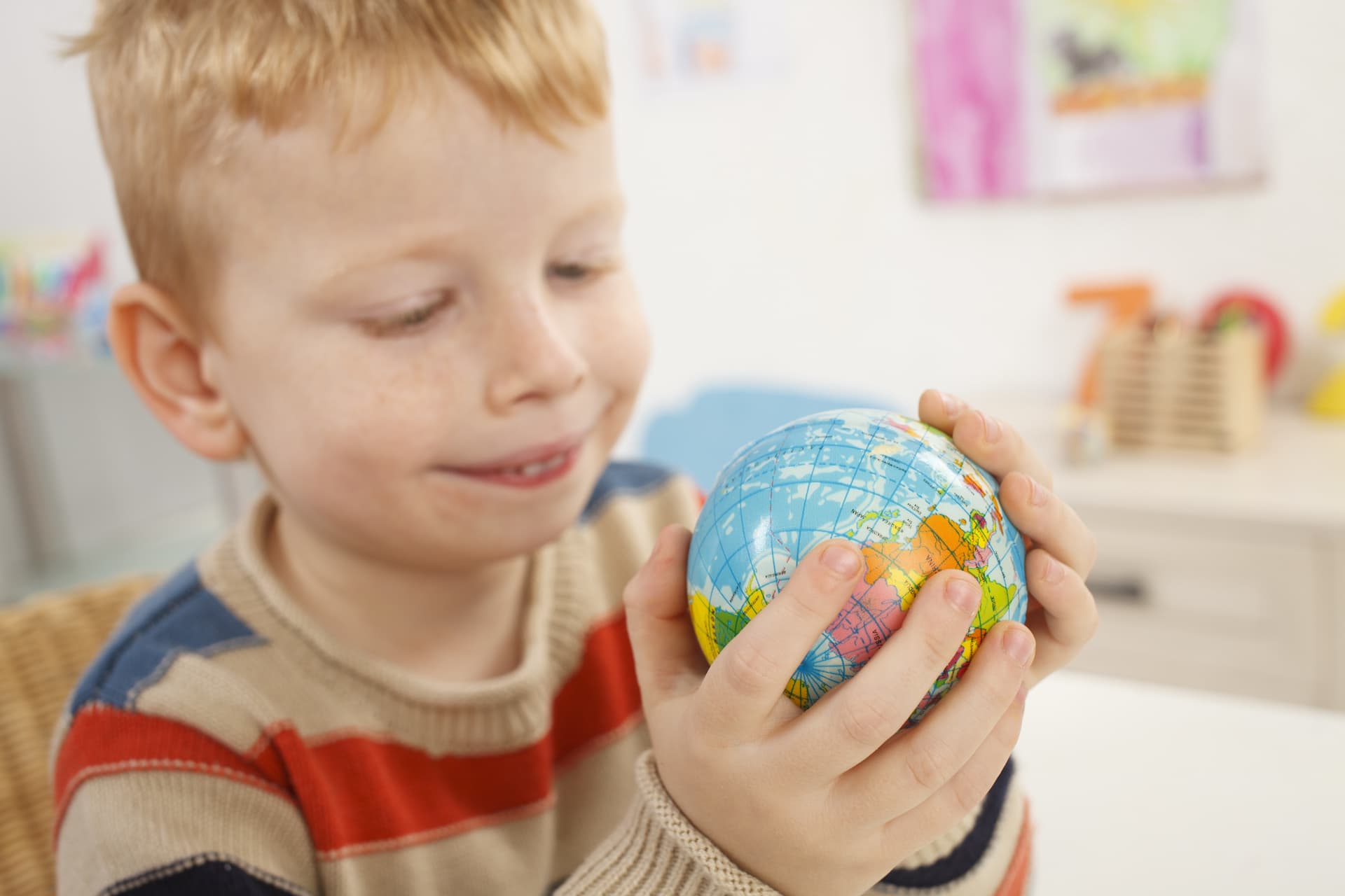 A young boy holding and smiling at a small globe of the world