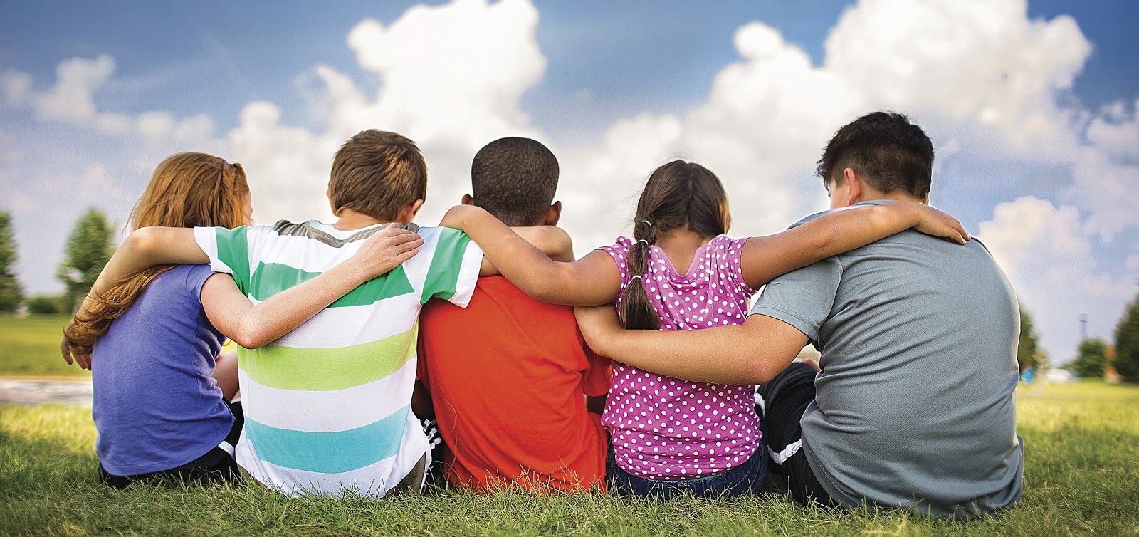 Group of kids arm in arm, sitting in the grass, watching the sunset.