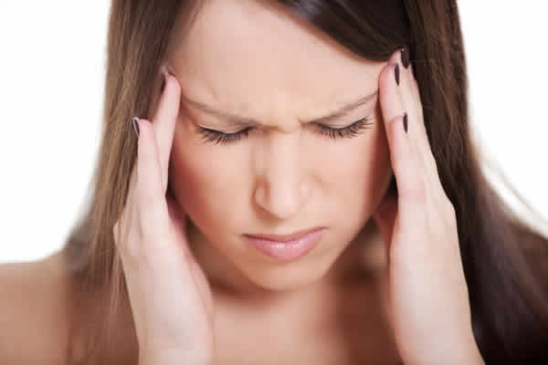 Young brunette grimacing and holding her head because of sinus pain caused by allergies.
