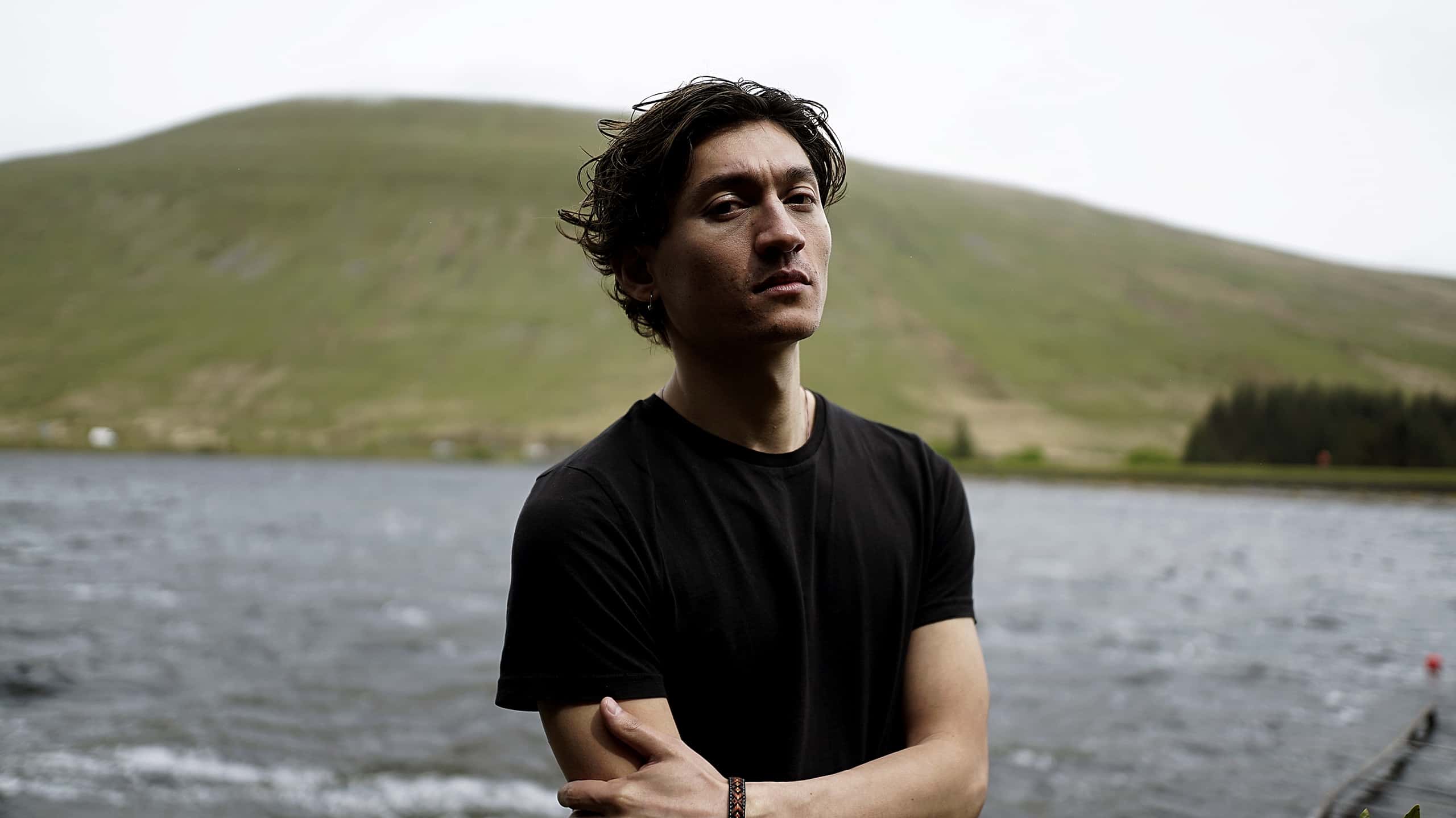 Photo of man with medium brown hair with arms crossed in front of a lake