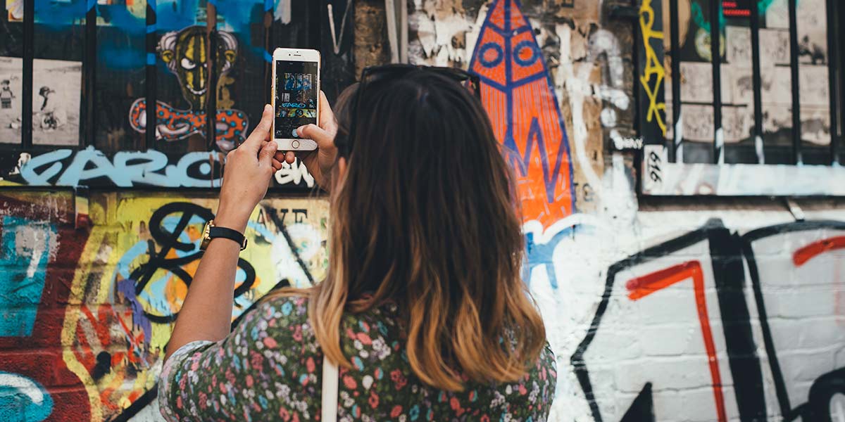 A person taking photos on a phone of graffiti on a wall