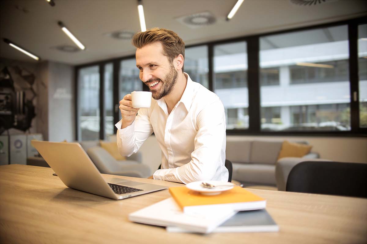 Man smiling drinking coffee in front of laptop
