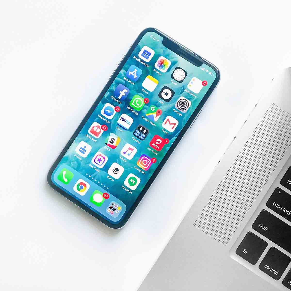 Phone next to Macbook with lots of apps on the home screen