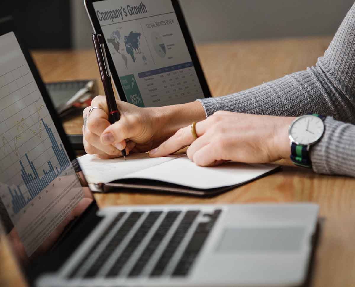 Woman looking at business graphs and writing in a notebook