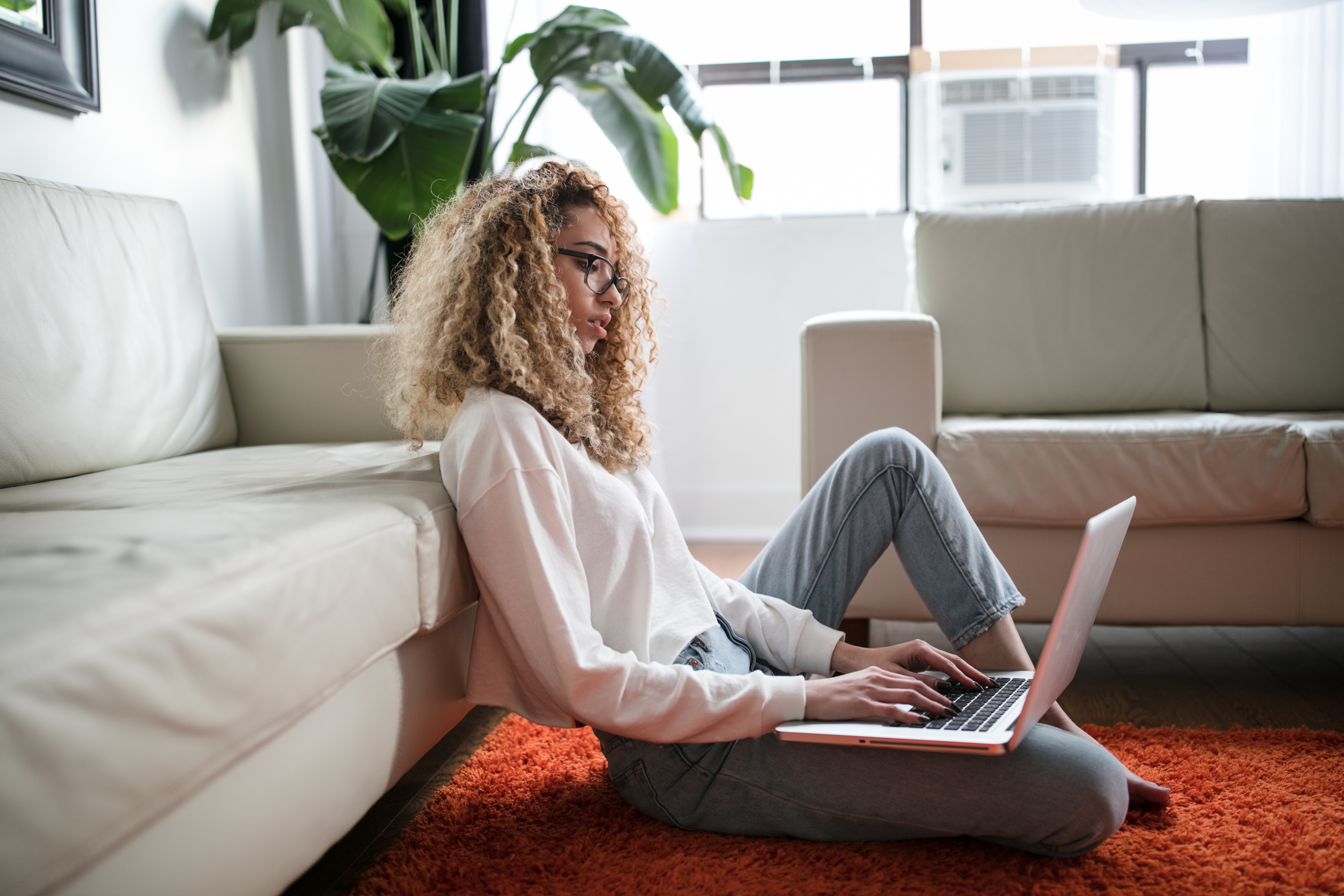 woman sitting on orange carpet typing on here keyboard