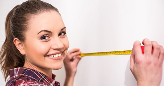 smiling woman holding measuring tape up to wall