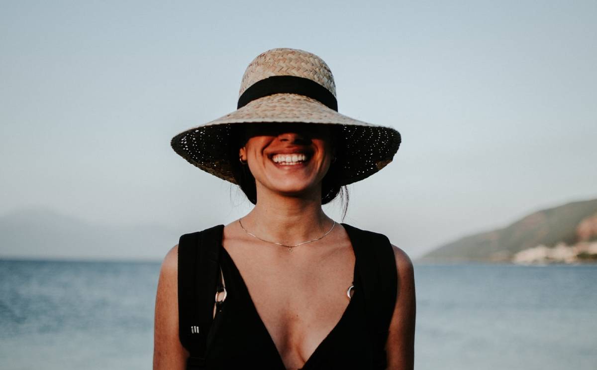 smiling woman in hat standing in front of beach