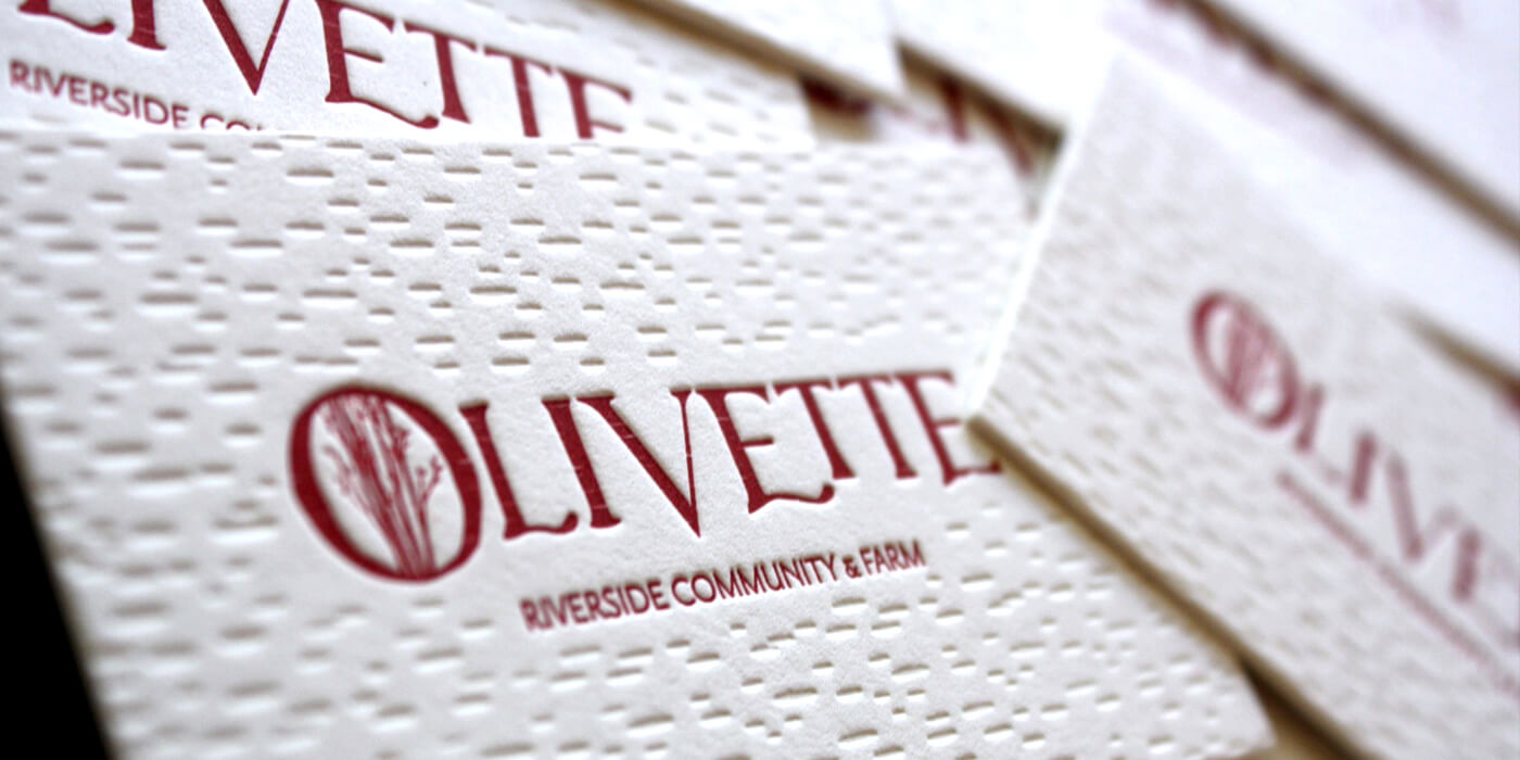 Olivette Riverside Community business card detail shows letter-pressed offwhite cards with deep imprint of birch bark texture and red spot-print logo.