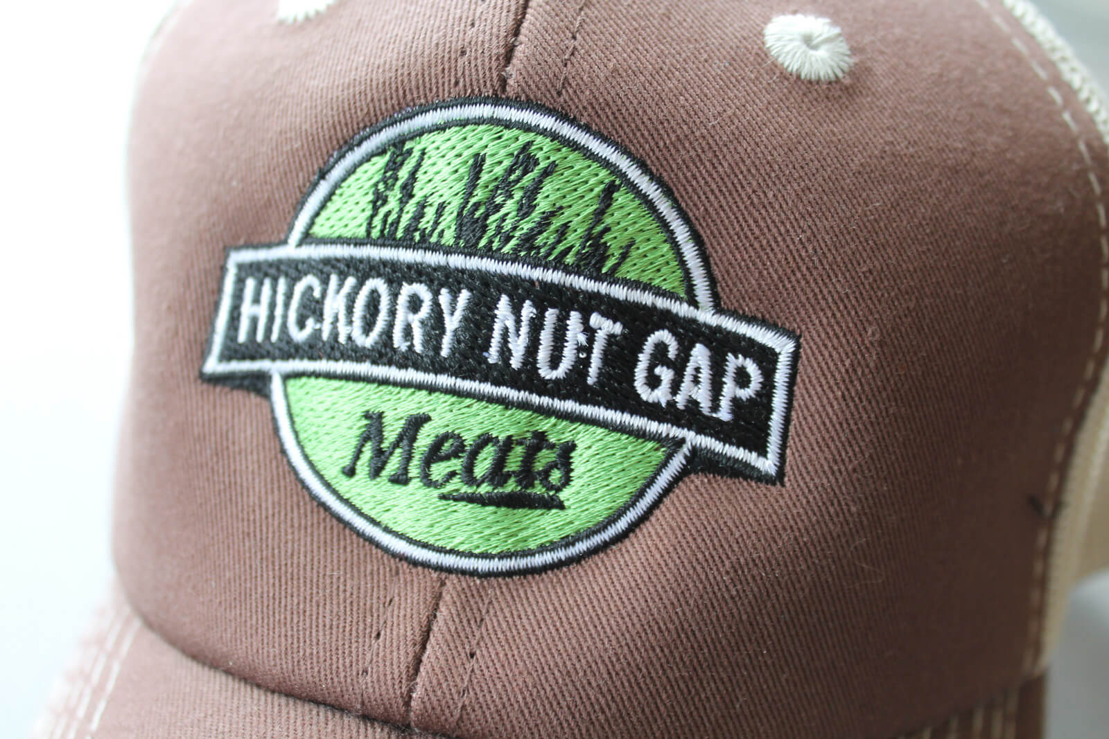 Green and black Hickory Nut Gap Meats logo embroidered on a brown and white hat.