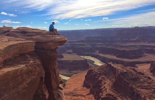 Person sitting on edge of cliff overlooking Utah mountains