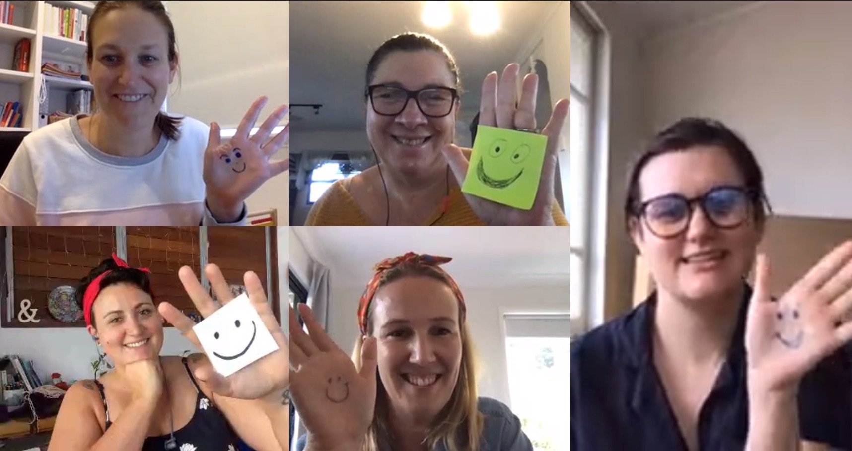 Members of The Social Deck team waving at the camera with smiley faces drawn on their hands for National Volunteer Week.