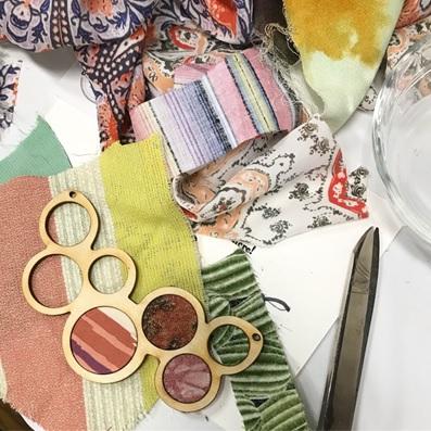 close up of fabric pieces on table with partially finished wood necklace on top.