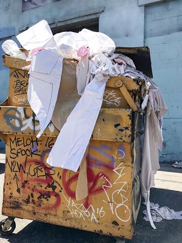 Yellow dumpster with graffiti on the side. Overflowing with fabric and paper patterns