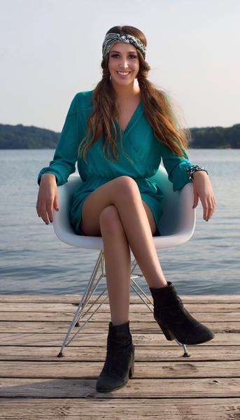 Girl sitting on a chair with a lake behind her. She's wearing a teal romper with back booties and a Regenerous Designs big braided headband.