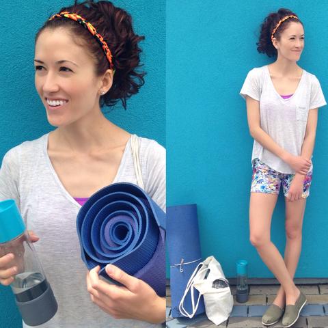 Yoga girl posing with her yoga matt and glass water bottle. She's wearing TOMs slip on shoes, colorful spandex shorts, light grey t-shirt, neon orange Regenerous Designs button band headband.
