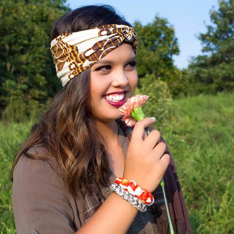 Girl in khaki green top with Regenerous Designs bullet shell bracelets, brown plaid infinity scarf, and orange big braided headband.