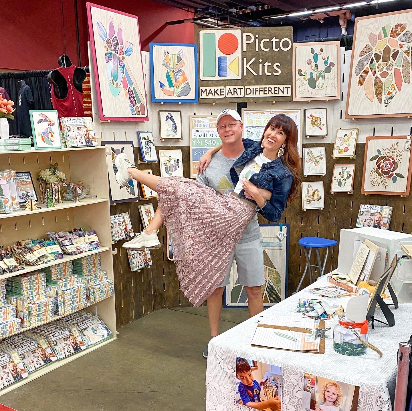 Nick Bahash holding Alyssa Bird in their Picto Kit Art booth setup at a craft event