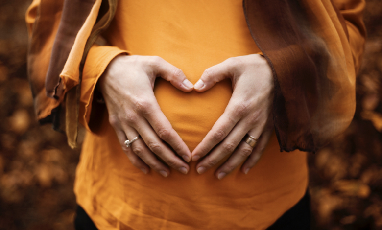 Pregnant women in organge clothes with hands over bump in heart sign