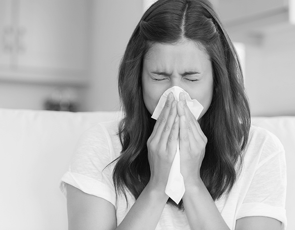 Woman suffering from non-allergic rhinitis holding a white tissue to her runny nose