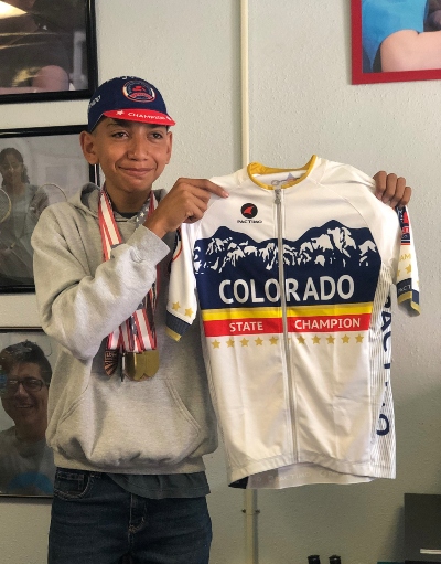 Francisco smiling while holding his Colorado State Championship Jersey and wearing all his cycling medals