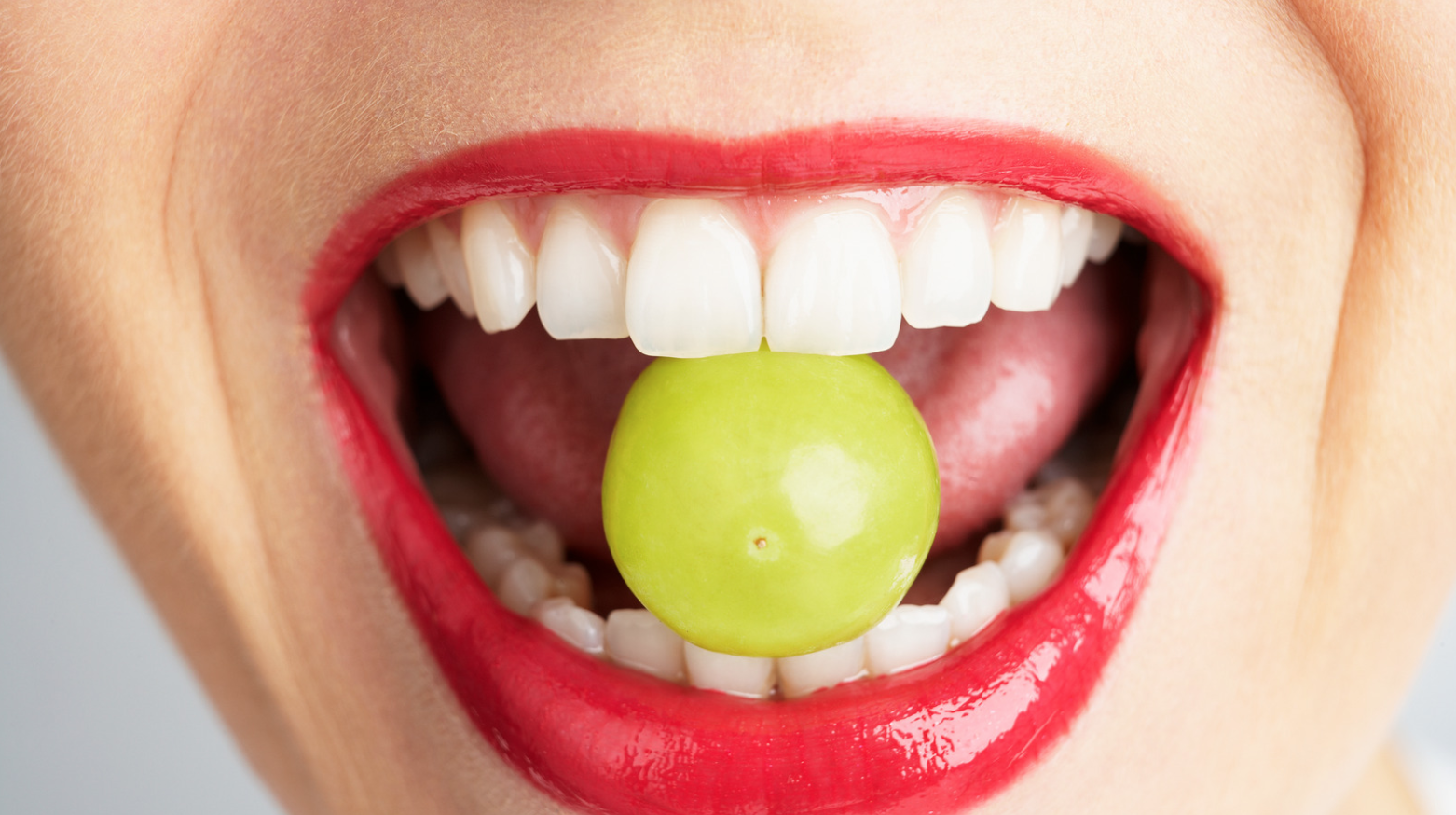 Upclose of woman with lipstick biting a grape