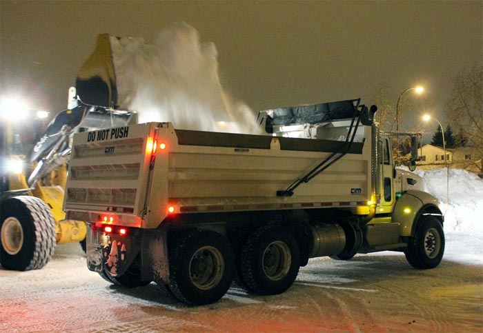 Heavy machine dumping snow into the back of a dump truck