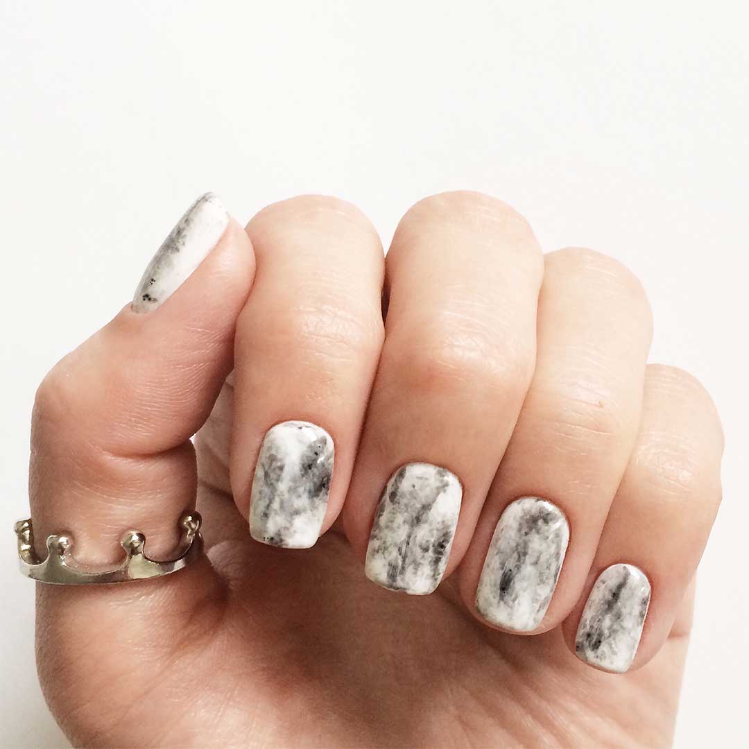 Manicured finger nails with white and grey marble design. Small crown ring on thumb.