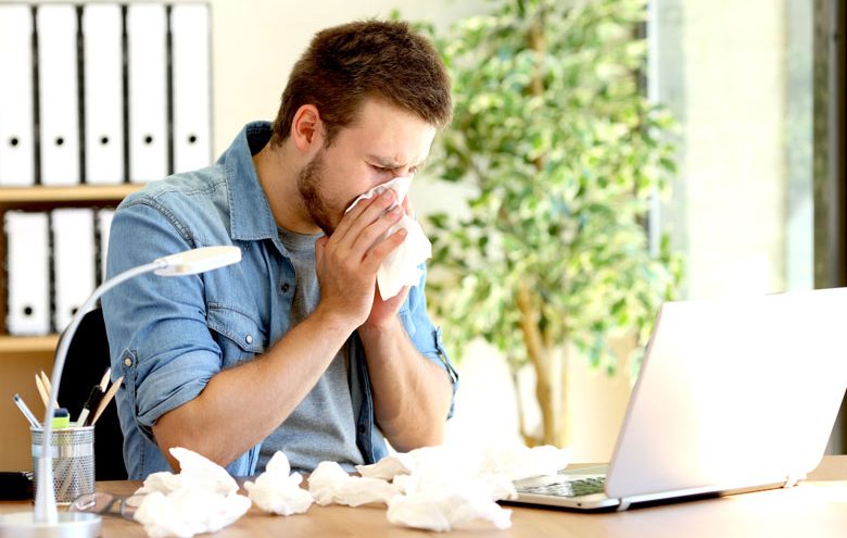 Man sitting on an office desk wiping his nose