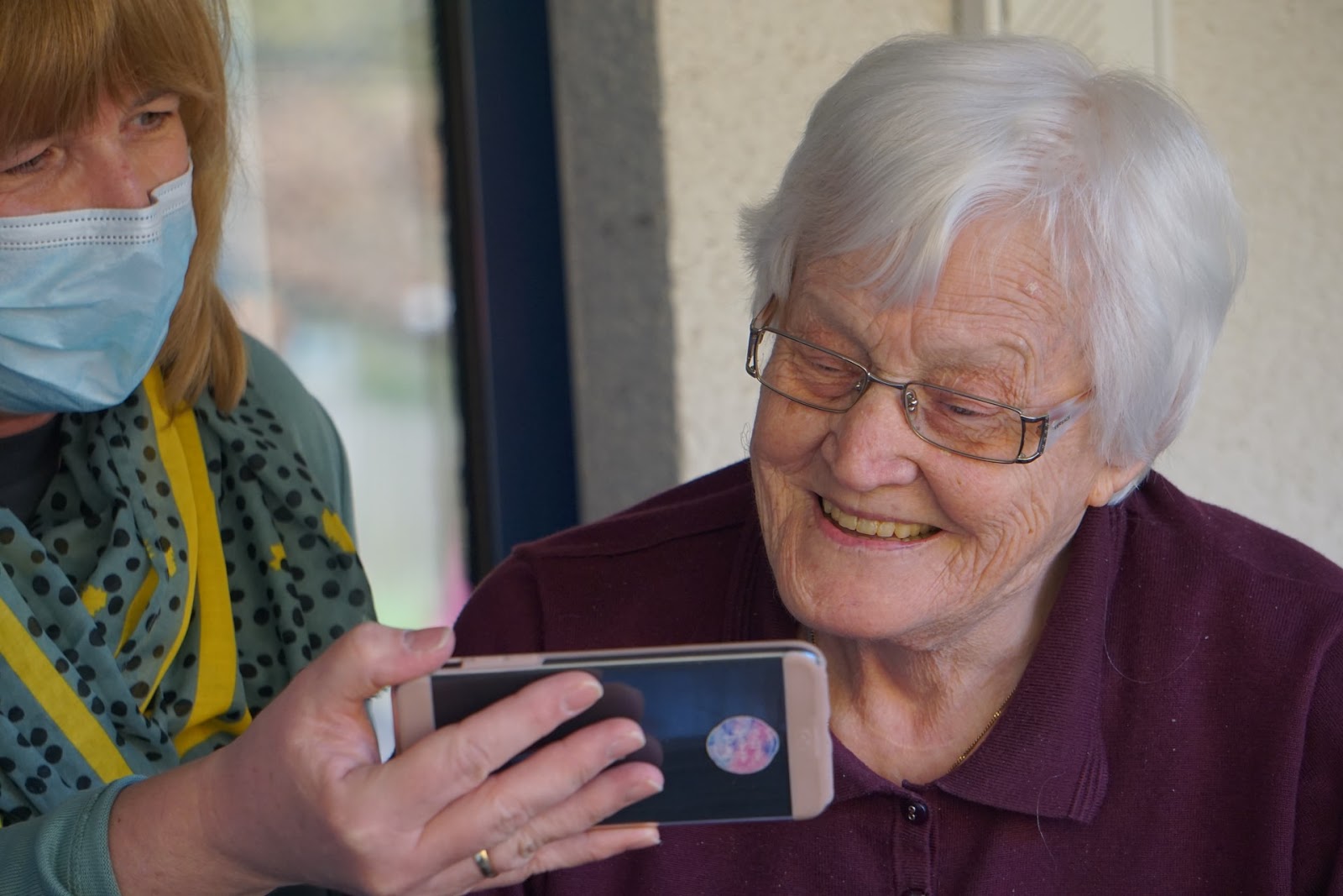 healthcare worker showing elderly worker something on her cell phone