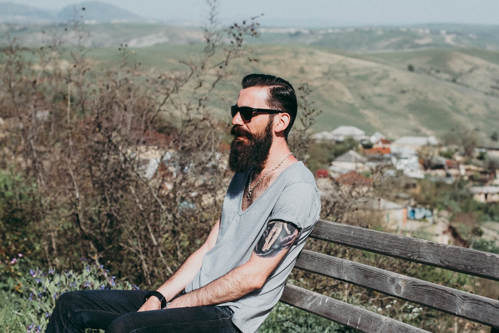 A man with a beard sitting alone on a bench.