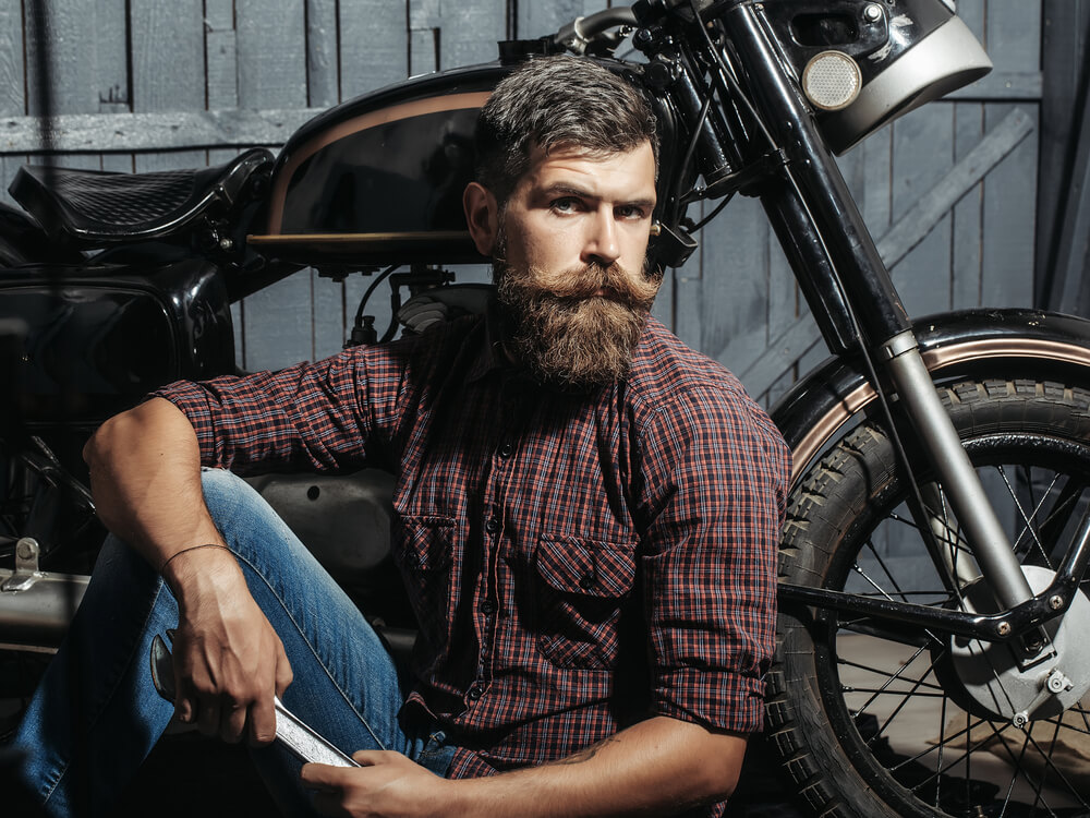 A man with a huge beard sitting in front of a motocycle.